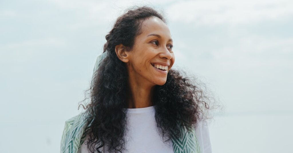 A joyful young woman with curly hair smiles brightly while enjoying the outdoors.